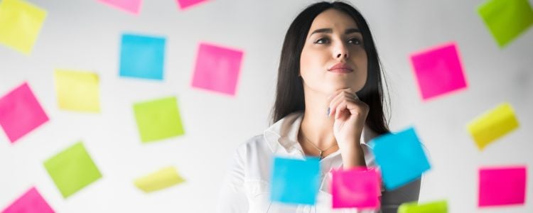 Mujer viendo notas adhesivas de colores pegadas en una ventana mientras hace una lluvia de ideas y piensa para hacer ejercicios y desarrollar la creatividad