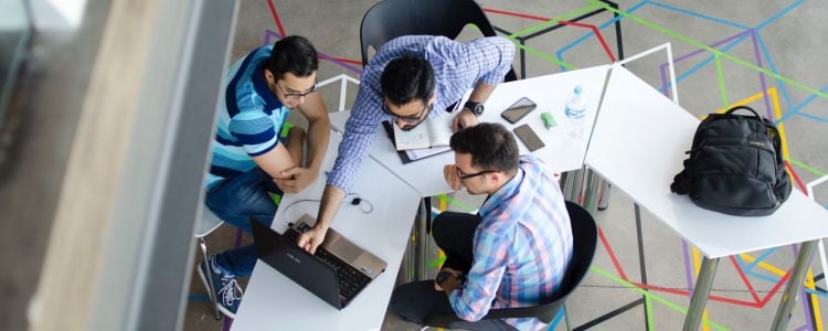 Hombres trabajando y hablando en una mesa sobre las razones para estudiar una maestría presencial